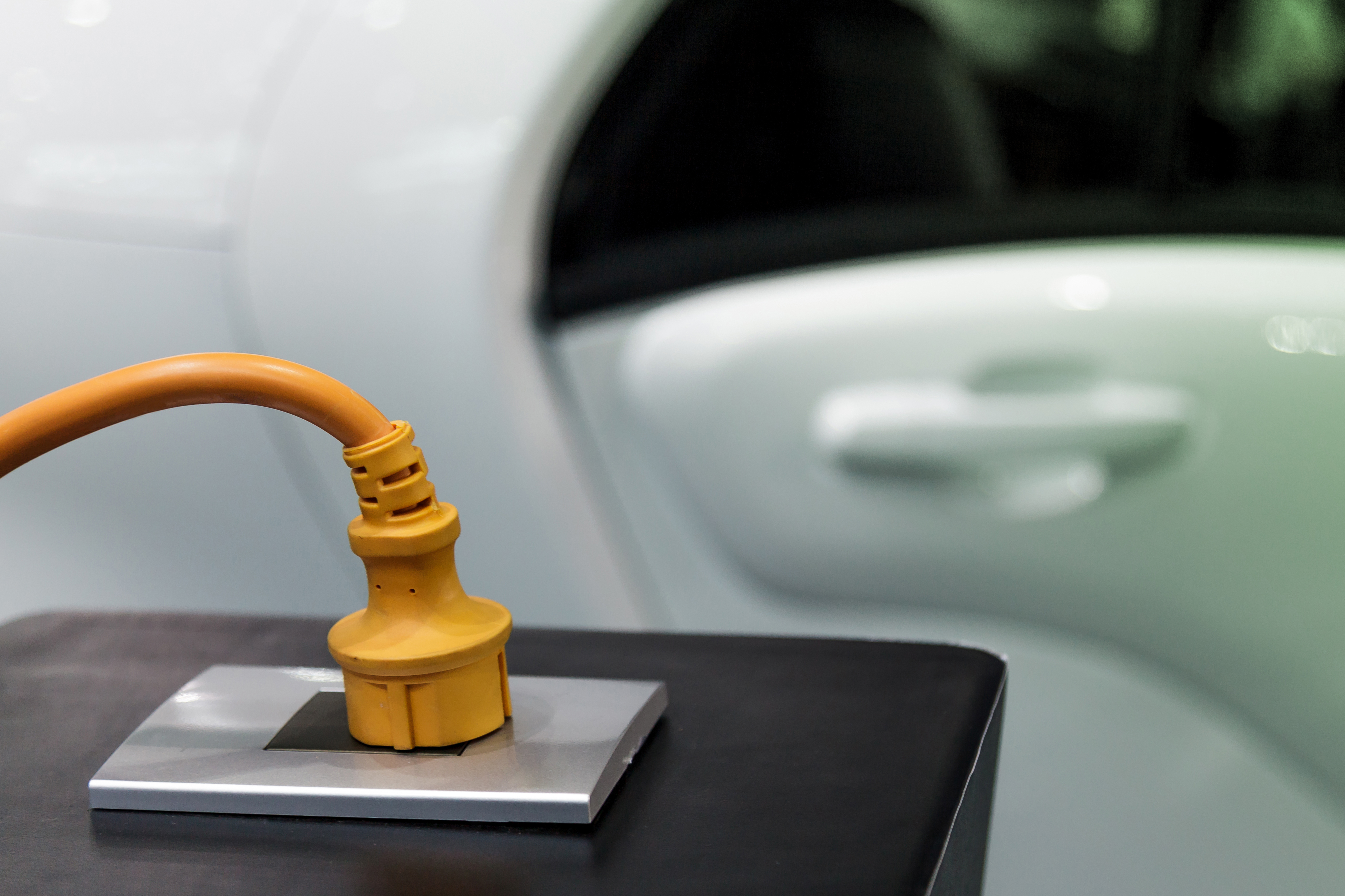 Ein Stecker in einer Steckdose vor einem E-Auto
